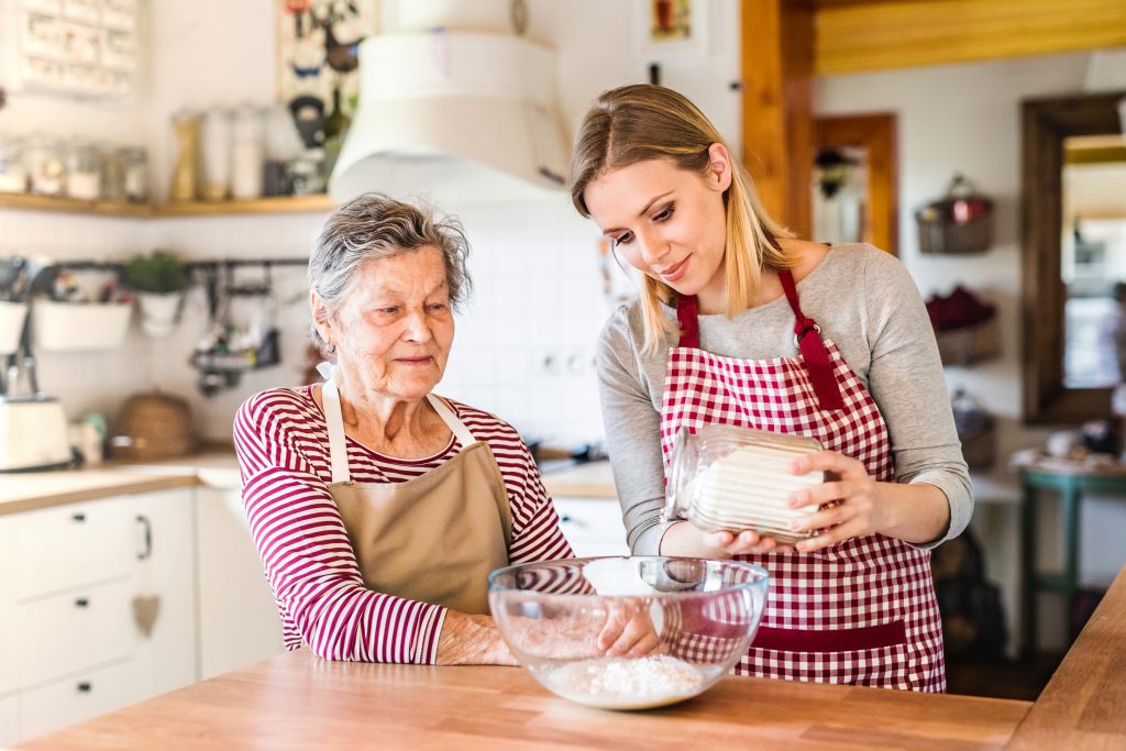 Caregiver assisting a senior in baking at home.